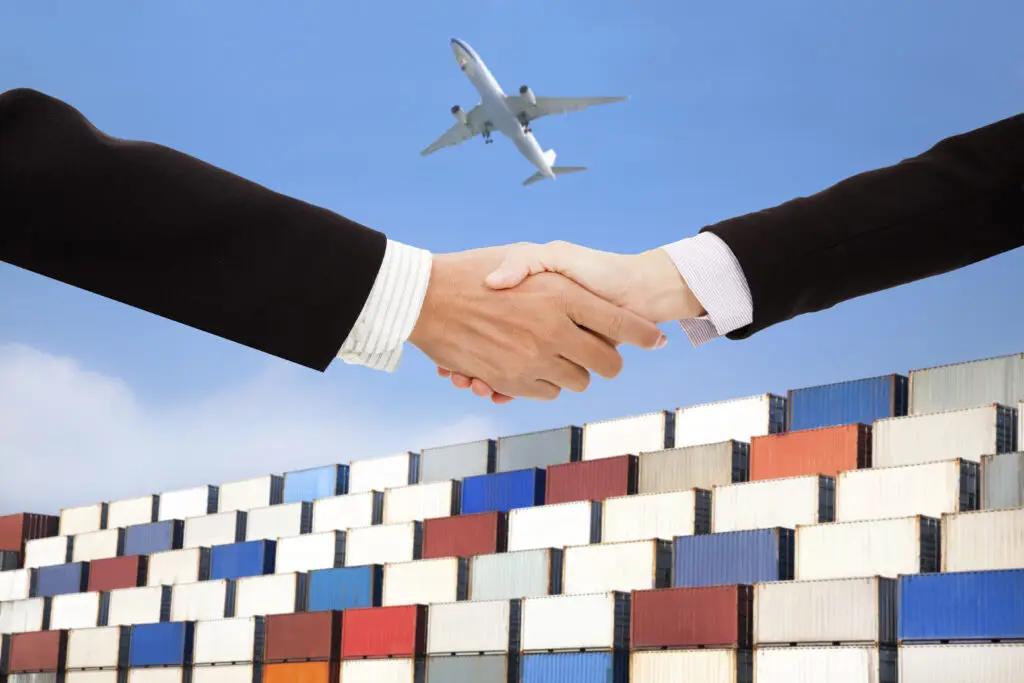 Business handshake with cargo containers and airplane in background, symbolizing international export agreement and global trade partnership.