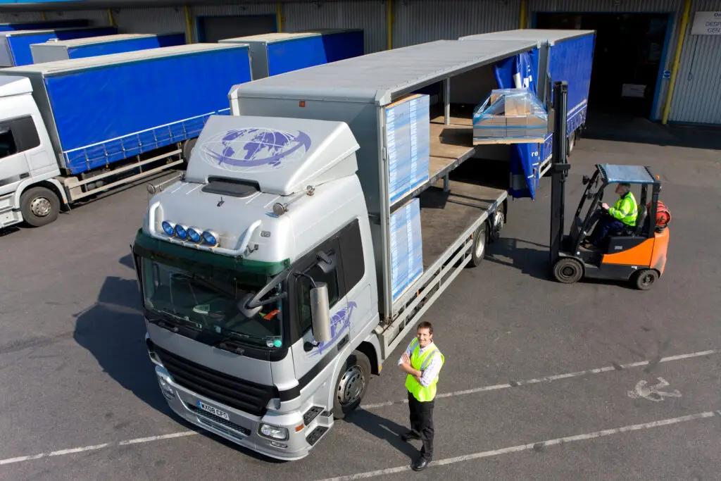 Forklift loading container collection onto road freight truck at logistics center, representing efficient trucking operations and cargo handling.