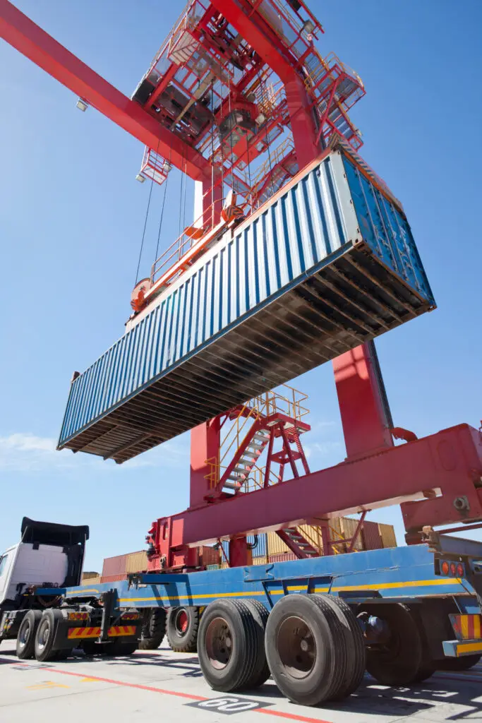Seafreight container being loaded onto a truck by a crane at a shipping terminal, showcasing international ship container logistics and transport of containers