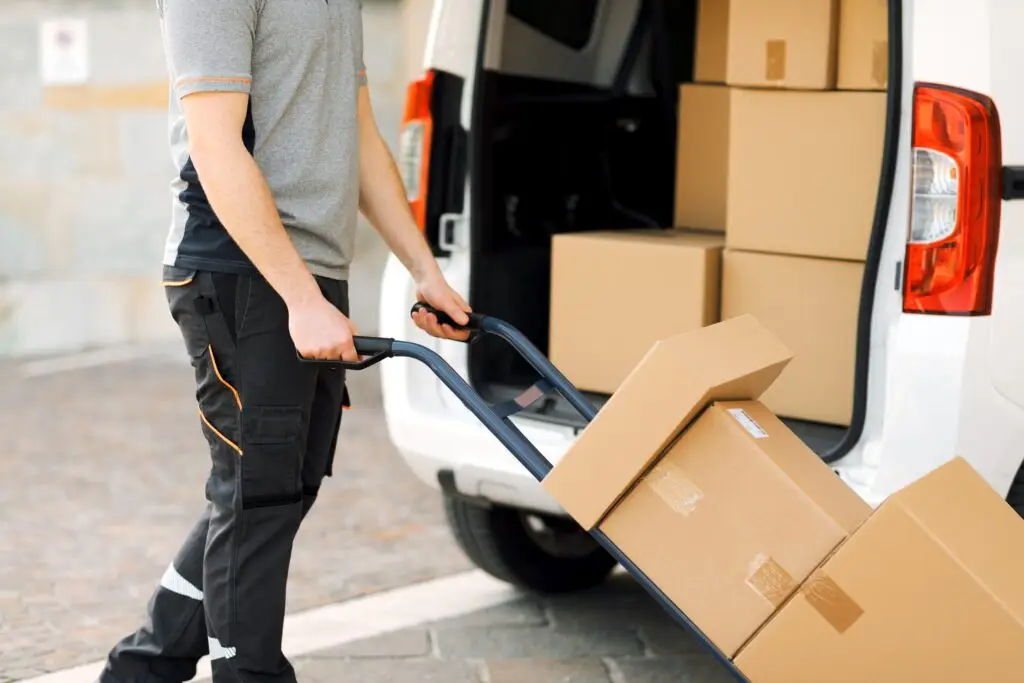 Delivery worker unloading bulk parcels from van using hand truck for last-mile logistics and parcel distribution.
